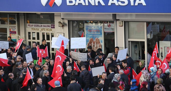 People stage a protest against the seizure of the Islamic Bank Asya, in front of a Bank Asya branch in downtown Ankara on February 4, 2015. Turkey on February 4 defended the seizure of an Islamic bank allied to an arch-foe of President Recep Tayyip Erdogan, the latest crackdown against US-exiled cleric Fethullah Gulen. Bank Asya has suffered major losses since last year after becoming embroiled in a bitter feud between Erdogan and his former ally Gulen, whom the president accuses of seeking to overthrow him. The placard (C) reads "boxes of money were not enough, now it's time to attack Bank Asya".  AFP PHOTO / ADEM ALTAN        (Photo credit should read ADEM ALTAN/AFP/Getty Images)