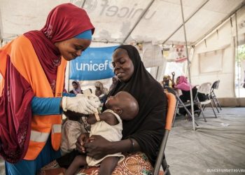 On 17th November 2016, UNICEF Nutrition Officer, Aishat Abdullahi, assesses 7 month old Umara Bukar for malnutrition at a UNICEF supported health clinic at Muna Garage IDP camp, Maiduguri, Borno State, northeast Nigeria as Umaras mother (in black) looks on.  20 days ago Umara weighed just 4.2kg when he first arrived at the health clinic run in partnership with the Nigerian government.  He now weighs 5.1kg.
To date, over 117,00 children with severe acute malnutrition (SAM) in northeast Nigeria have been admitted to therapeutic feeding programmes run by UNICEF and partners.

In November 2016, Fanna Mohammed is worried about her son. 7-month old Umara is thin and listless. He rests his head against his mother's shoulder as she carries him in her arms. The family fled their village in a rural areas of Borno state earlier this year due to the ongoing Boko Haram-related crisis.  Now they live in an IDP camp in the state capital, Maiduguri. Muna Garage IDP camp is home to an estimated 20,000 people. 8,000 of those are children under the age of 5.  Fanna says Umara's been ill for the past few week. He is physically showing signs of severe acute malnutrition. The bones on his chest and back are prominent; his skin is loose around his arms and legs. Fanna's brought Umara to a UNICEF-supported medical clinic that's situated within the camp. Umara is immediately given life-saving treatment. Ready-to-Use Therapeutic Food (RUFT) is a peanut-based paste that's high in calories and full of added vitamins and minerals. Three packets a day, for eight weeks can save the life of a child with severe acute malnutrition. Lying in his mother's arms, Umara slowly but surely eats the food. Before he's allowed home, the health team put him on a course of extra vitamin A, antibiotics and anti-malarial medicine.  A week later, Umara's back at the clinic for his second screening. There's a small, but steady improvement. His arm is plumper, at 9.7CM and he's put on a little weight. The