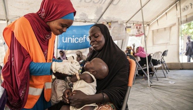 On 17th November 2016, UNICEF Nutrition Officer, Aishat Abdullahi, assesses 7 month old Umara Bukar for malnutrition at a UNICEF supported health clinic at Muna Garage IDP camp, Maiduguri, Borno State, northeast Nigeria as Umaras mother (in black) looks on.  20 days ago Umara weighed just 4.2kg when he first arrived at the health clinic run in partnership with the Nigerian government.  He now weighs 5.1kg.
To date, over 117,00 children with severe acute malnutrition (SAM) in northeast Nigeria have been admitted to therapeutic feeding programmes run by UNICEF and partners.

In November 2016, Fanna Mohammed is worried about her son. 7-month old Umara is thin and listless. He rests his head against his mother's shoulder as she carries him in her arms. The family fled their village in a rural areas of Borno state earlier this year due to the ongoing Boko Haram-related crisis.  Now they live in an IDP camp in the state capital, Maiduguri. Muna Garage IDP camp is home to an estimated 20,000 people. 8,000 of those are children under the age of 5.  Fanna says Umara's been ill for the past few week. He is physically showing signs of severe acute malnutrition. The bones on his chest and back are prominent; his skin is loose around his arms and legs. Fanna's brought Umara to a UNICEF-supported medical clinic that's situated within the camp. Umara is immediately given life-saving treatment. Ready-to-Use Therapeutic Food (RUFT) is a peanut-based paste that's high in calories and full of added vitamins and minerals. Three packets a day, for eight weeks can save the life of a child with severe acute malnutrition. Lying in his mother's arms, Umara slowly but surely eats the food. Before he's allowed home, the health team put him on a course of extra vitamin A, antibiotics and anti-malarial medicine.  A week later, Umara's back at the clinic for his second screening. There's a small, but steady improvement. His arm is plumper, at 9.7CM and he's put on a little weight. The