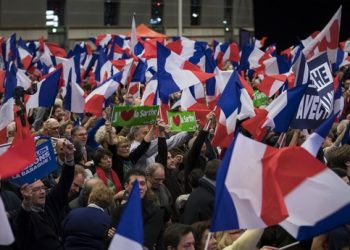 epa05647742 People wave French flags as candidate for the right-wing Les Republicains (LR) party primaries ahead of the 2017 presidential election and former French Prime Minister, Francois Fillon delivers a speech during the nation anthem during a political rally of the second round of the rightwing presidential primary, in Paris, France, 25 November 2016. Francois Fillon took a commanding lead in the two-round primary that is widely expected to decide the country's next leader. The second round will be held on 27 November 2016.  EPA/IAN LANGSDON