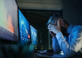 Frustrated and worried businessman with computer sitting at desk, working late. Financial crisis concept.