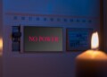 Electrical switch box panel with the text "no power" and burning candle in hand Concept of "green energy" crisis in Europe