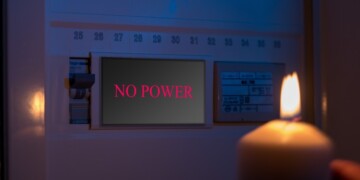 Electrical switch box panel with the text "no power" and burning candle in hand Concept of "green energy" crisis in Europe