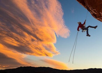 Female climber rappelling down a sheer cliff.