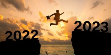 2023 new year concept, new year card.Silhouette of a businessman jumping on a cliff in 2023 over sea cliff at a beautiful sunset. business plan and success for 2023.