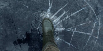 Fisherman foot on broken cracked thin ice at lake. Dangerous fishing