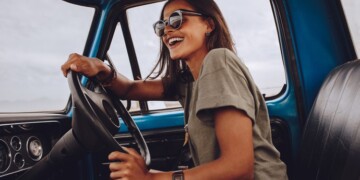Portrait of young woman having fun while driving a car. Cheerful woman going on a road trip on a old truck.
