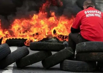 Flames and smoke rise from burning tyres as a worker sits on a barricade blocking the entrance of U.S. tyre-maker Goodyear's plant to protest job cuts in Amiens, northern France, in this June 3, 2013 file picture. French trade unionists held two executives overnight on Tuesday January 7, 2014 at the country's Goodyear tyre plant - a flashpoint for France's troubled industrial relations - to demand higher pay-outs for more than a thousand planned layoffs. Workers at the idled factory in the northern city of Amiens have been trying to negotiate redundancy terms with management for nearly a year, after Texan tyre tycoon Maurice Taylor withdrew a potential rescue bid on the grounds that French workers were lazy - triggering a political storm.  The message reads "Goodyear - Gangster Bosses".  Picture taken June 3, 2013.  REUTERS/Benoit Tessier/Files  (FRANCE - Tags: BUSINESS INDUSTRIAL EMPLOYMENT)