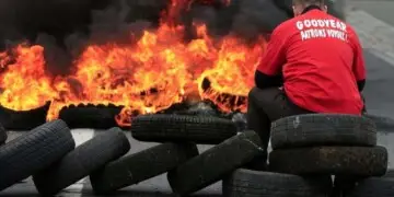 Flames and smoke rise from burning tyres as a worker sits on a barricade blocking the entrance of U.S. tyre-maker Goodyear's plant to protest job cuts in Amiens, northern France, in this June 3, 2013 file picture. French trade unionists held two executives overnight on Tuesday January 7, 2014 at the country's Goodyear tyre plant - a flashpoint for France's troubled industrial relations - to demand higher pay-outs for more than a thousand planned layoffs. Workers at the idled factory in the northern city of Amiens have been trying to negotiate redundancy terms with management for nearly a year, after Texan tyre tycoon Maurice Taylor withdrew a potential rescue bid on the grounds that French workers were lazy - triggering a political storm.  The message reads "Goodyear - Gangster Bosses".  Picture taken June 3, 2013.  REUTERS/Benoit Tessier/Files  (FRANCE - Tags: BUSINESS INDUSTRIAL EMPLOYMENT)