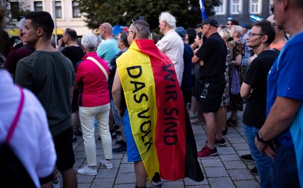 A man covering with a German national flag with the slogan "We are the people" listens to Bjoern Hoecke, top candidate of the far-right Alternative for Germany party, or AfD, during an election campaign rally of the party for upcoming state elections in Suhl, Germany, Tuesday, Aug. 13, 2024. (AP Photo/Markus Schreiber)