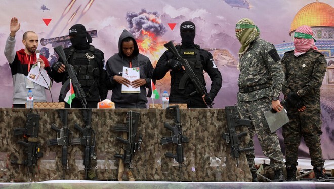 Israeli hostages Averu Mengistu (4th-R) and Tal Shoham (L) are flanked by Hamas fighters as they stand on a stage during their release in Rafah in the southern Gaza Strip on February 22, 2025. Masked militants paraded Tal Shoham and Averu Mengistu on stage in the southern Gazan city of Rafah before handing them over to officials from the Red Cross. (Photo by Omar AL-QATTAA / AFP)