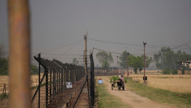 An Indian farmer carries harvested cattle feed on a horse cart near fencing at the India-Pakistan international border in Ranbir Singh Pora, outskirts of Jammu, India, Monday, April 28, 2025. (AP Photo/Channi Anand)
