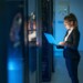 Woman IT specialist in elegant suit working on notebook computer in data center next to server racks