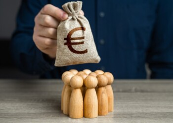 A man is holding a euro money bag over a group of people figurines. Generation of funds from cooperation. Organization of the community budget. Payment for labor and services. Political lobbying.