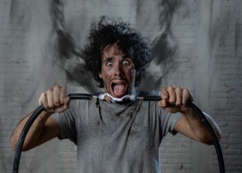 Man getting electric shock connecting broken electrical cables at home. Husband having domestic accident being electrocuted with dirty burnt face and crazy expression. Electricity DIY repairs danger.