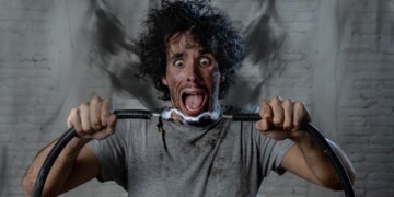 Man getting electric shock connecting broken electrical cables at home. Husband having domestic accident being electrocuted with dirty burnt face and crazy expression. Electricity DIY repairs danger.