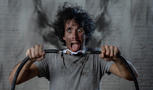 Man getting electric shock connecting broken electrical cables at home. Husband having domestic accident being electrocuted with dirty burnt face and crazy expression. Electricity DIY repairs danger.